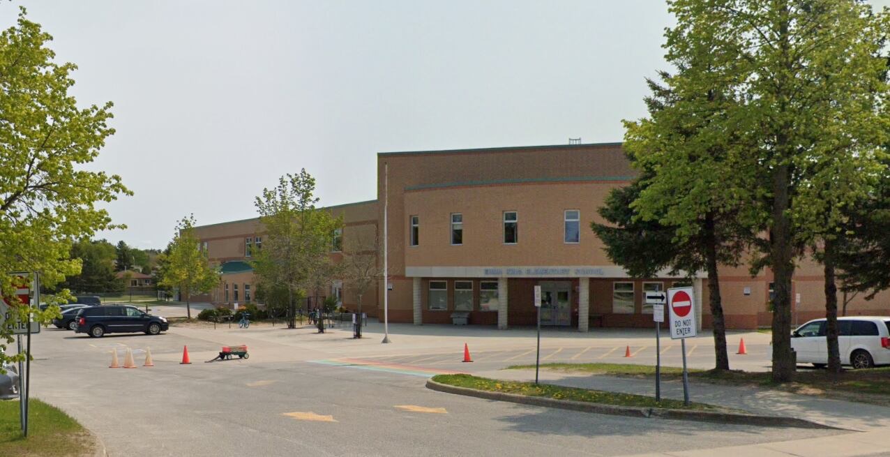 Emma King Elementary School — two-storey brick school behind mature trees, with the bus loop in the foreground