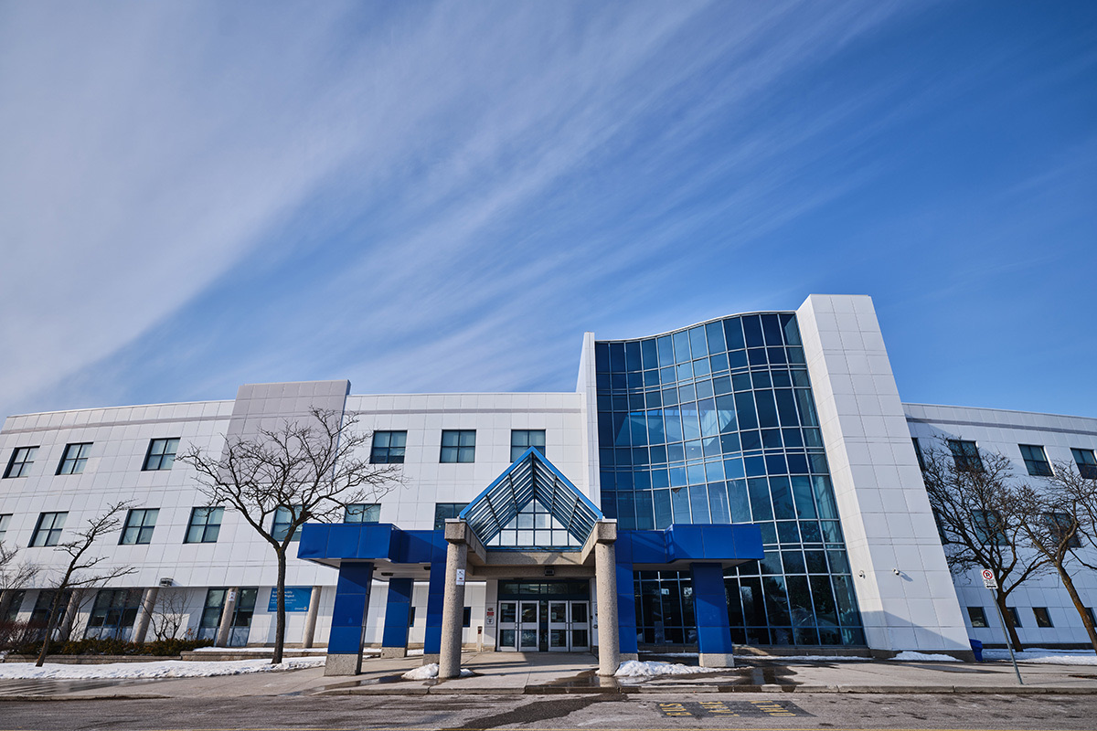 Dr. J.M. Denison Secondary School — white three-storey building with a curved blue glass entrance tower